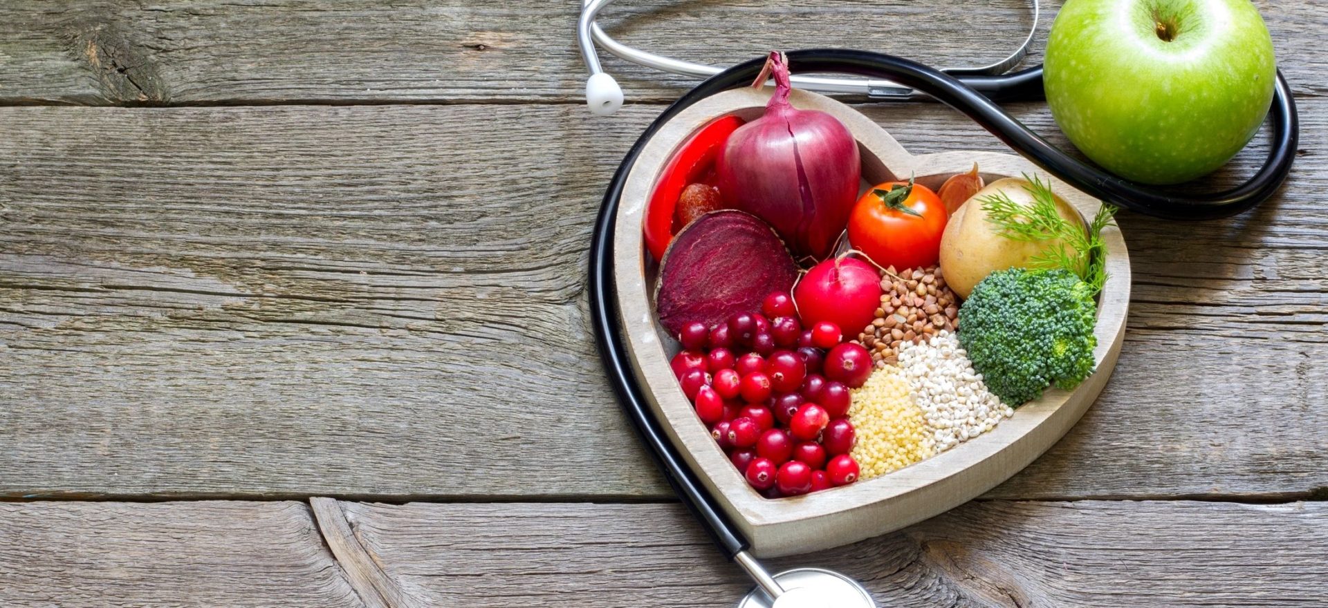 Life to the Fullest: Picture of wood background with heart-shaped container filled with different colorful fruits and vegetables surrounded by a stethoscope